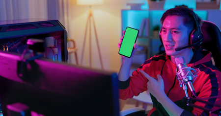 asian man internet celebrity have a live stream and show app on the smartphone with green screen at homeの写真素材