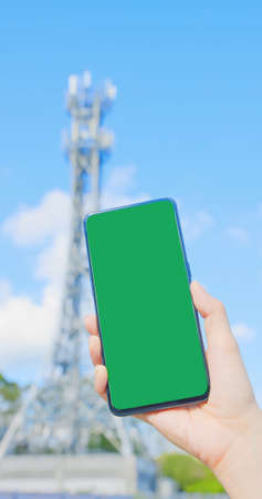 woman holds smartphone with green screen near 5G base stationの写真素材