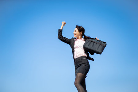Smiling Asian businesswoman looking forward and clenching fist like winner with isolated sky blue backgroundの写真素材
