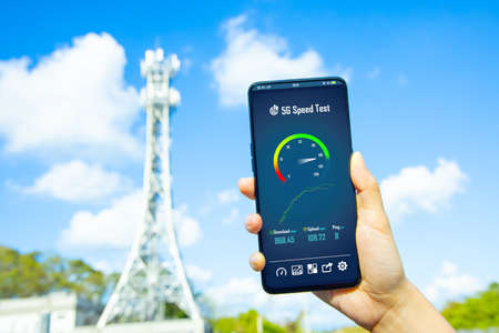 woman holds smartphone with 5g speed test near base stationの写真素材