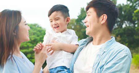asian father holding little boy with mom happily in the parkの写真素材