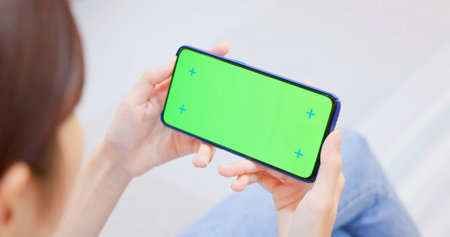 rear view of asian woman look at green screen smartphone in the living room at homeの写真素材