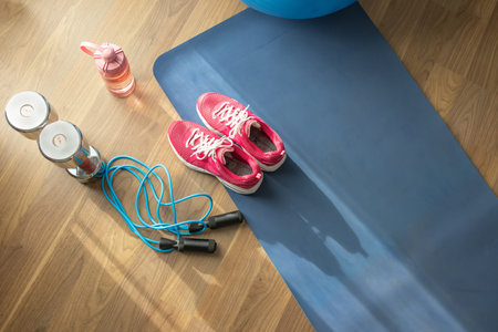 top view set of sports equipment include dumbbell and jump rope with sneakers on yoga Mat in house
