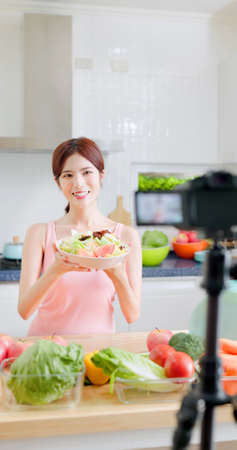 asian Fitness woman records training on vegetarian cooking-Distances diet through camera video tutorialの写真素材