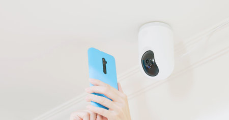 female homeowner is installing surveillance cameras on ceiling and setting app by mobile phone at...