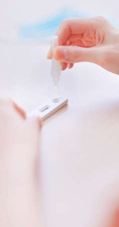 Covid-19 rapid home test kit-close up view of asian woman drops put into a test cartridgeの写真素材