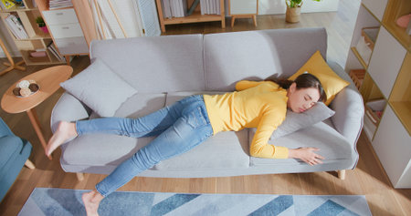 Overhead View of asian woman lying buried her face in couch feels tired in living room at homeの写真素材