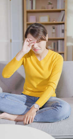 Asian woman rubbing her eyes by hands in the living room at homeの写真素材