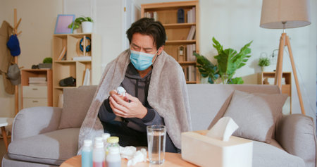 sick asian man having fever and measuring body temperature with ear thermometer in living room at...