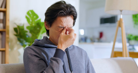 asian man rubbing his eyes by hands in the living room at home