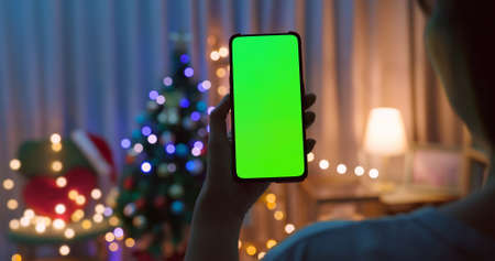 rear of asian woman watch green screen smartphone with christmas decoration and tree at homeの写真素材