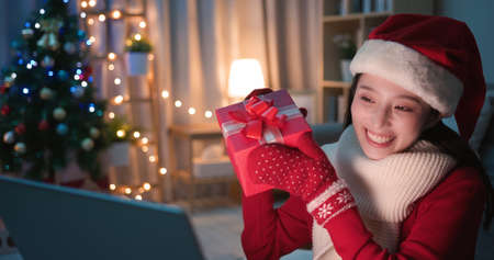 asian young woman wearing christmas clothes has video chat on digital tablet and shows present box to her friendの写真素材