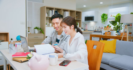 asian young couple calculate expenses finance with laptop and discuss plan together at home happilyの写真素材