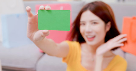close up of happy asian woman shows green credit card on her hand with shopping bags at homeの写真素材