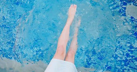 Closeup of woman legs and barefoot kicking and splashing water in the poolの写真素材