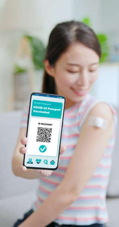 Asian young woman showed her Covid-19 digital vaccine passport on smartphone after she vaccinated in living room at homeの写真素材