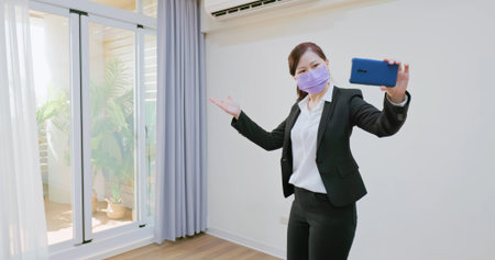 real estate agent wearing protective face mask to prevent COVID-19 has video chat with customers by...