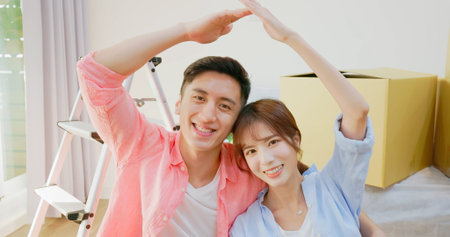 slow motion of happy young asian couple hold keys of new house in close up - they sitting on wooden floor with many boxes are looking at cameraの写真素材