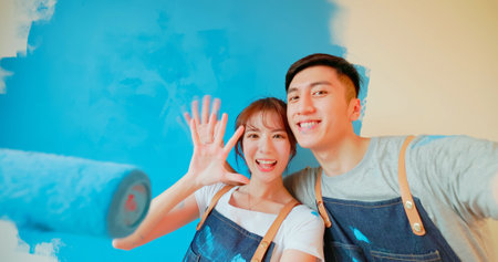 young asian couple decorate home - they take selfie by mobile phone while painting wall with blue colorの写真素材