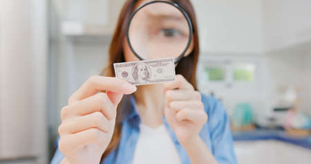 inflation concept - worried asian woman find money is getting smaller by magnifier at kitchenの写真素材