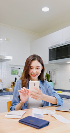 asian woman checks social media from mobile phone at kitchenの写真素材