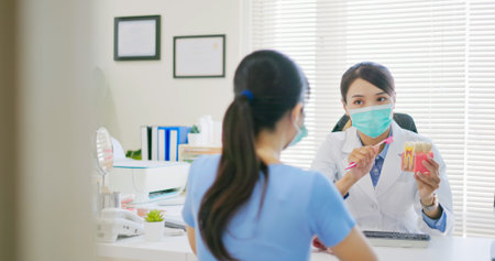 asian female dentist teaches patient for teeth brushing and tooth decay by denture model while they...