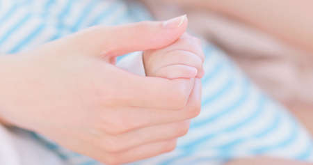 authentic shot of mom holding baby hand gently in close upの写真素材