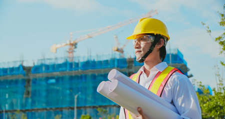 asian male architect with technical drawing works on construction siteの写真素材