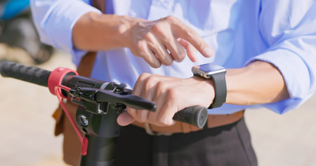 keyless security concept - close up of asian businessman starts electric scooter by smart watch...