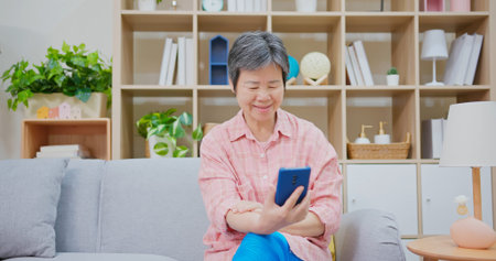 asian senior woman sitting on couch use smart phone at home