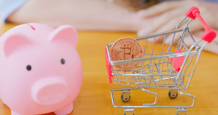 close up of businesswoman with bitcoin in small shopping cart and piggy bank in office