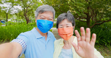 Authentic shot of asian elderly couple wearing face mask have video chat by mobile phone happily outdoorの写真素材
