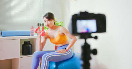 Asian Fitness woman records training workout biceps and triceps muscle with dumbbell - Distances exercise through digital camera video tutorialの写真素材