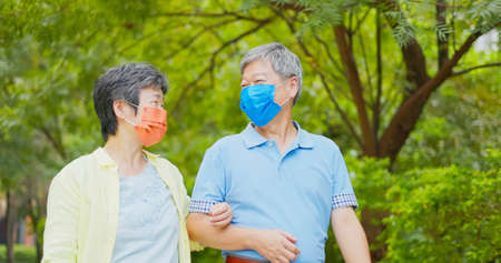 Authentic shot of asian elderly couple wearing face mask walk happily outdoorの写真素材