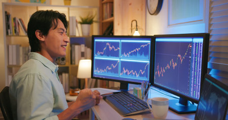 asian man has stock market or cryptocurrency investment from home by computer and he is excited...