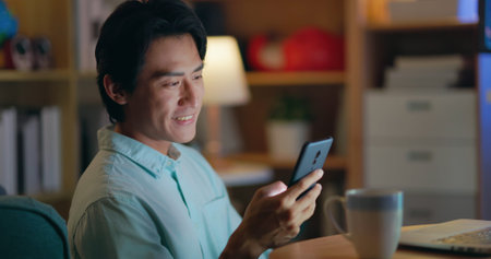 asian man sitting on the floor is using phone and laptop at night in his room