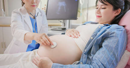 asian female doctor exams a pregnant woman lying in hospital ward by stethoscopeの写真素材