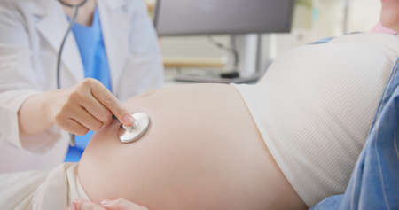 close up of asian female doctor exams a pregnant woman lying in hospital ward by stethoscopeの写真素材