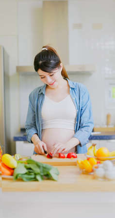 Vitamin C supplementation for Pregnancy - asian pregnant woman is preparing food and cutting tomato in kitchen at homeの写真素材
