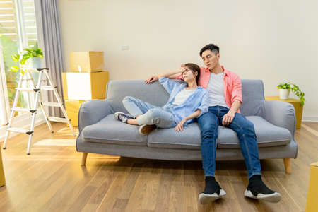 young asian couple are tired after moving into new home - they sit on sofaの写真素材