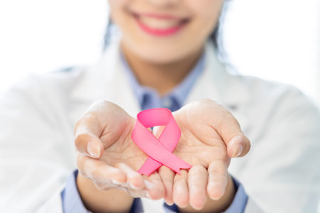 close up of smiling asian female doctor holds pink ribbon