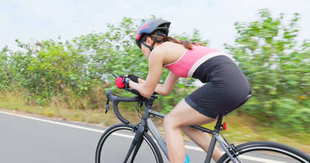 Triathlon bike training - back view of asian young woman wearing helmet is riding a bicycle on the road and enjoy sport or healthy lifestyle conceptの写真素材