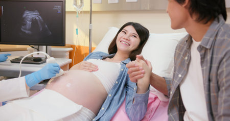 asian pregnant woman lying on bed has ultrasound scan with husband and doctor explains the results...