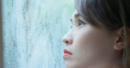 close up face of an asian lonely woman looking the rain falling through a window at home