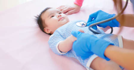authentic shot of asian mother and infant in pediatrics clinic - doctor examine baby health by stethoscope and infant lying on bedの写真素材