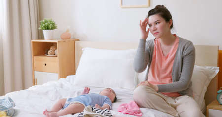 authentic shot of asian mother has postpartum depression with her baby who is lying on bedの写真素材