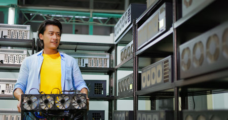 young asian man checking is holding crypto mining machine and checking other equipment with smile in factoryの写真素材