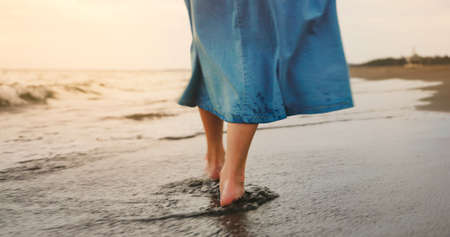 close up bare feet of asian woman wearing in blue skirt is walking at beachの写真素材