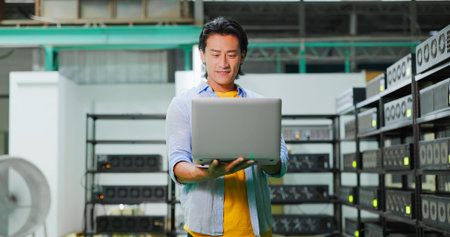 young asian man with smile is checking every crypto mining machine by laptop on his hand in factoryの写真素材