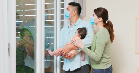 asian young parents hugging their child is wearing face mask and staying isolation at home for self quarantine due to epidemic of COVID19 - they look out the windowの写真素材